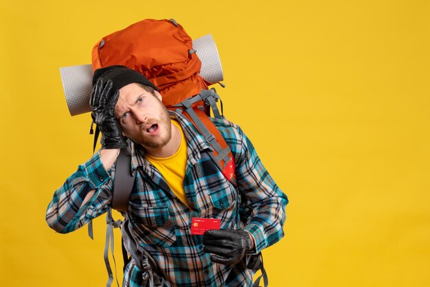 Vue de face du jeune homme agité avec backpacker holding carte de réduction