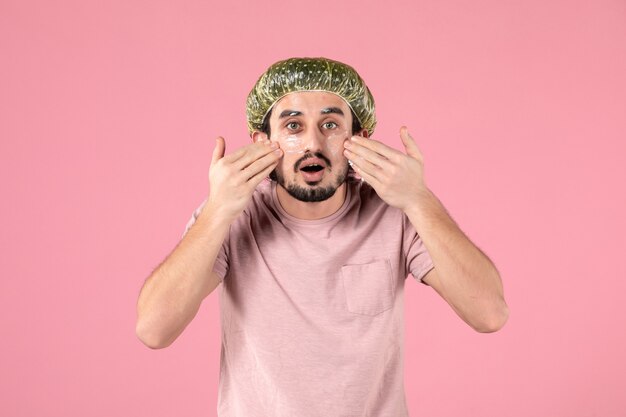 vue de face du jeune homme appliquant un masque sur son visage sur un mur rose