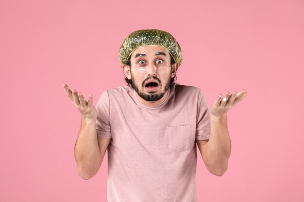 vue de face du jeune homme appliquant un masque sur son visage sur un mur rose