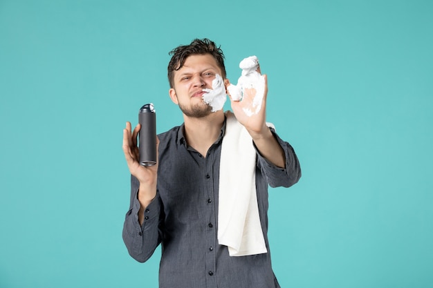 vue de face du jeune homme appliquant de la mousse pour se raser le visage sur le mur bleu