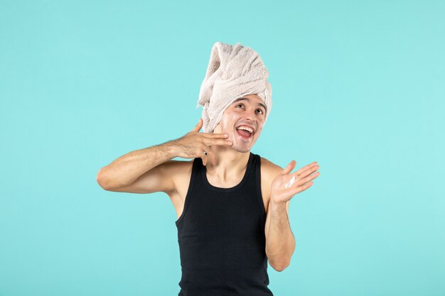 vue de face du jeune homme après la douche en appliquant de la crème sur son visage sur un mur bleu