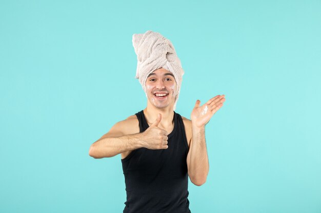 vue de face du jeune homme après la douche en appliquant de la crème sur son visage sur un mur bleu