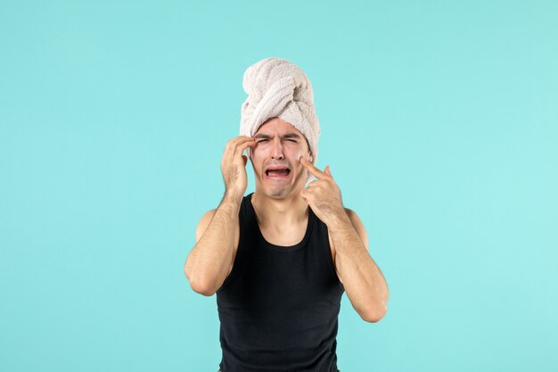 vue de face du jeune homme après la douche essayant de faire sortir le petit bouton pleurant sur le mur bleu