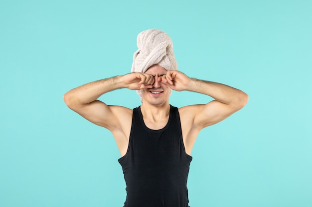 vue de face du jeune homme après la douche avec une serviette sur la tête sur le mur bleu