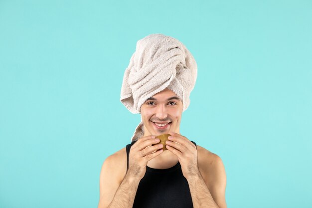 vue de face du jeune homme après la douche tenant des tranches de kiwi sur le mur bleu