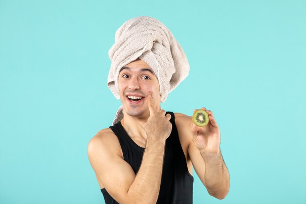 vue de face du jeune homme après la douche tenant des tranches de kiwi sur le mur bleu