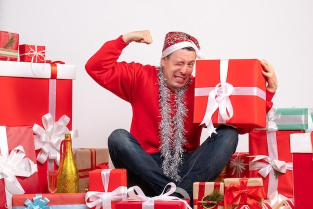Vue de face du jeune homme assis autour de cadeaux de Noël sur mur blanc