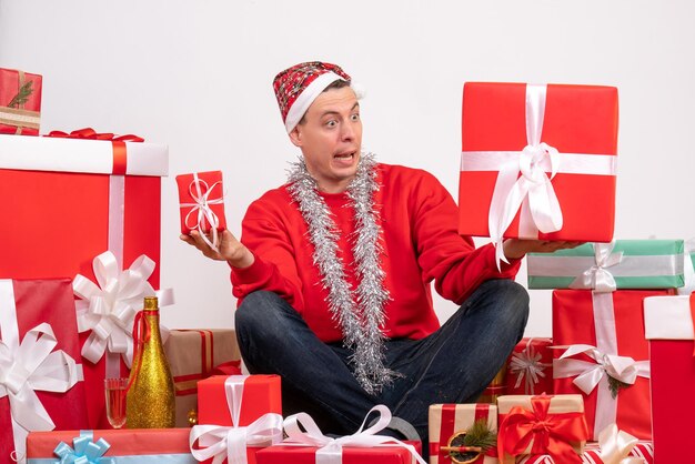 Vue de face du jeune homme assis autour de cadeaux de Noël sur mur blanc