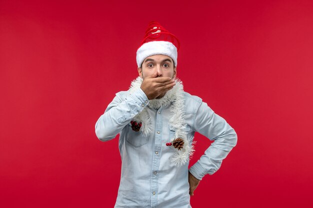 Vue de face du jeune homme au visage surpris sur le mur rouge