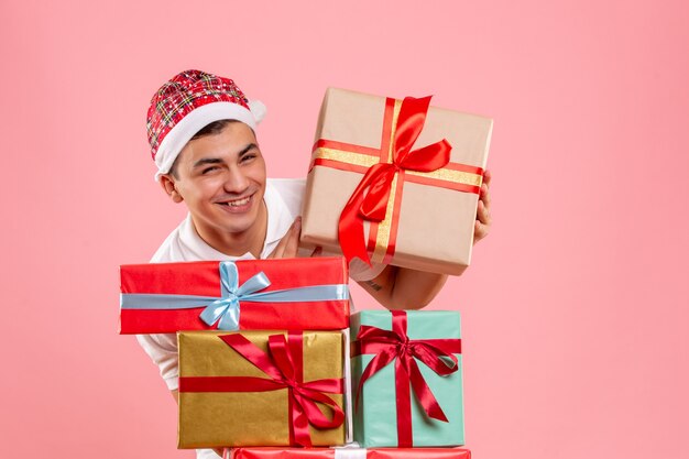 Vue de face du jeune homme autour de différents cadeaux de Noël sur le mur rose