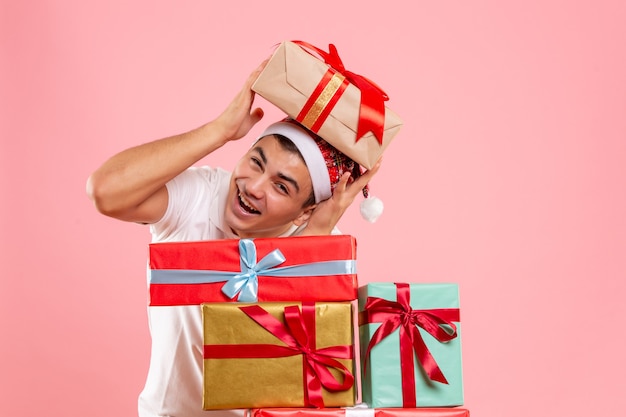 Vue de face du jeune homme autour de différents cadeaux de Noël sur le mur rose