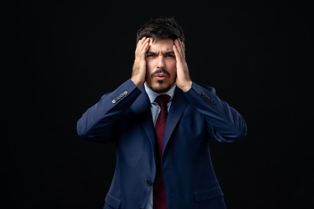 Vue de face du jeune homme barbu épuisé en costume sur un mur sombre isolé