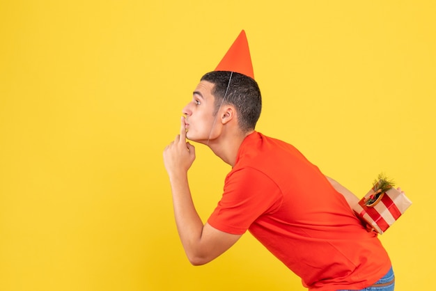 Vue De Face Du Jeune Homme Cachant Le Cadeau De Noël Derrière Son Dos Sur Le Mur Jaune