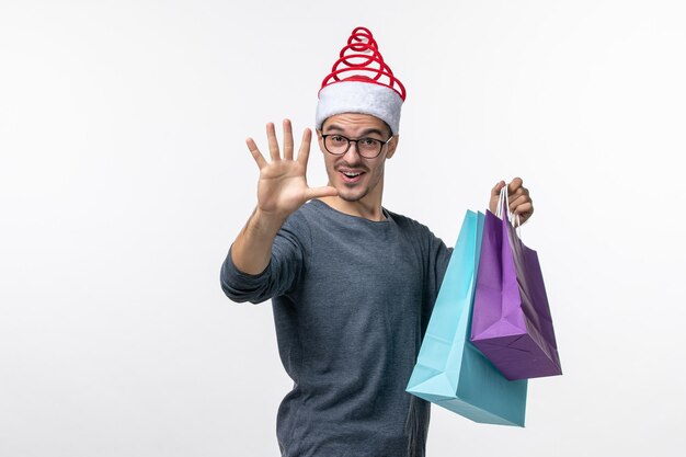 Vue de face du jeune homme avec des cadeaux après le shopping sur un mur blanc