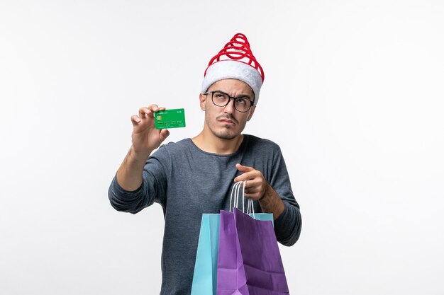 Vue de face du jeune homme avec des cadeaux et une carte bancaire sur un mur blanc