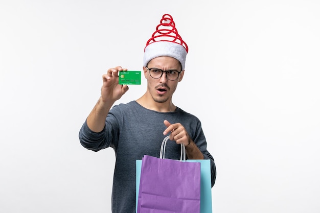 Vue de face du jeune homme avec des cadeaux et une carte bancaire sur un mur blanc