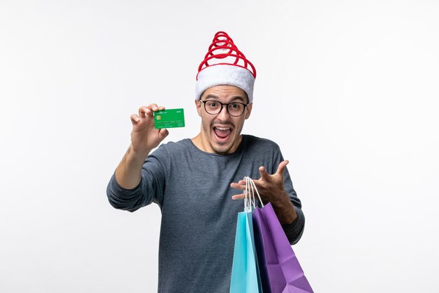 Vue de face du jeune homme avec des cadeaux et une carte bancaire sur un mur blanc