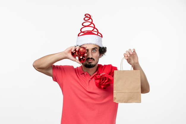 Vue de face du jeune homme avec des cadeaux et des jouets sur un mur blanc