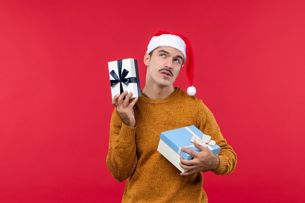 Vue de face du jeune homme avec des cadeaux sur le mur rouge