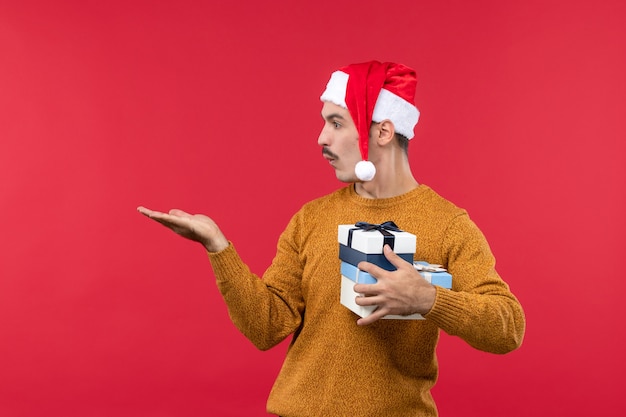 Vue de face du jeune homme avec des cadeaux sur le mur rouge