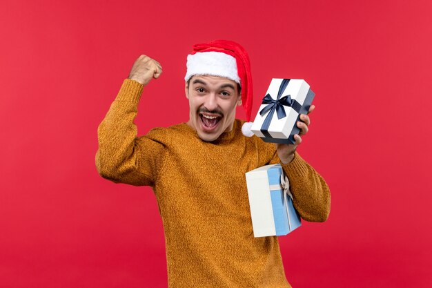 Vue de face du jeune homme avec des cadeaux sur le mur rouge