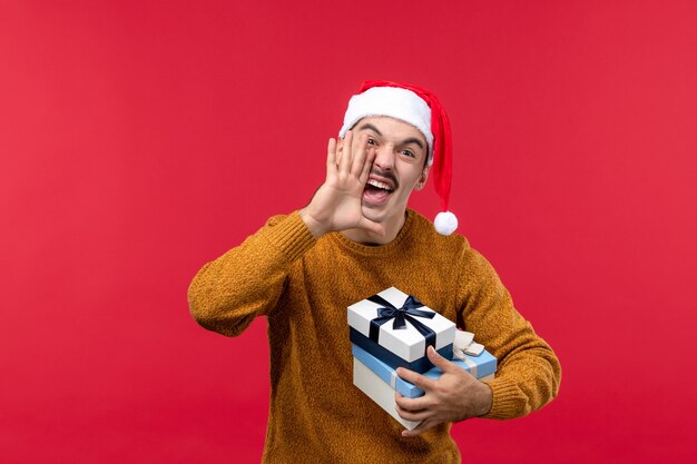 Vue de face du jeune homme avec des cadeaux sur le mur rouge