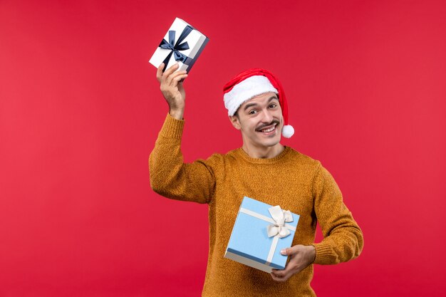 Vue de face du jeune homme avec des cadeaux sur le mur rouge