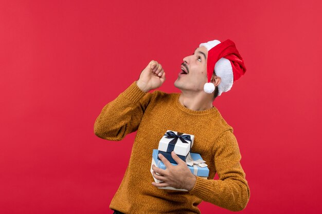 Vue de face du jeune homme avec des cadeaux de nouvel an sur le mur rouge