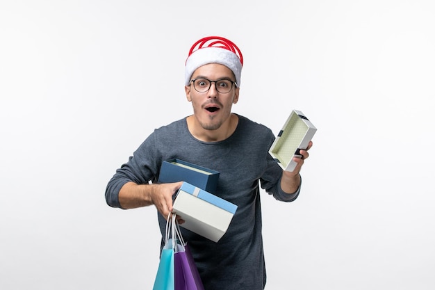 Vue de face du jeune homme avec des cadeaux de vacances sur mur blanc