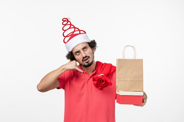 Vue de face du jeune homme avec des cadeaux de vacances sur mur blanc