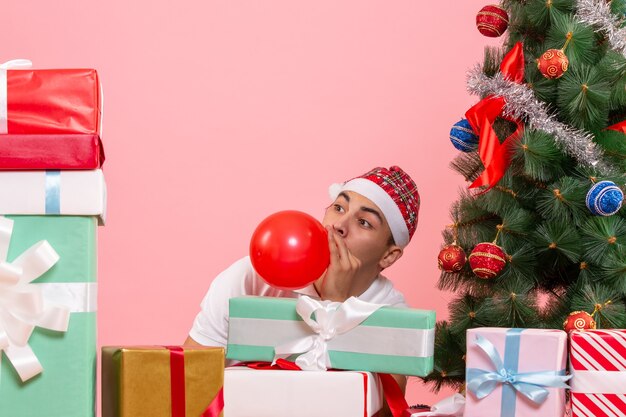 Vue de face du jeune homme célébrant Noël autour de cadeaux sur mur rose