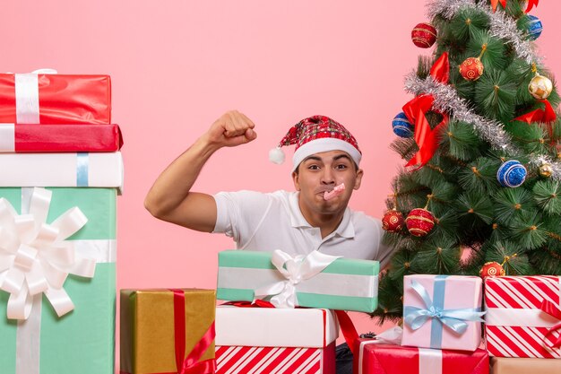 Vue de face du jeune homme célébrant Noël autour de cadeaux sur mur rose