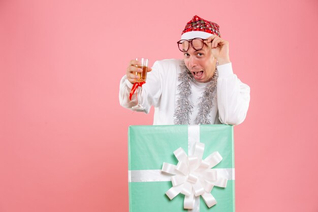 Vue de face du jeune homme célébrant Noël avec un verre sur le mur rose