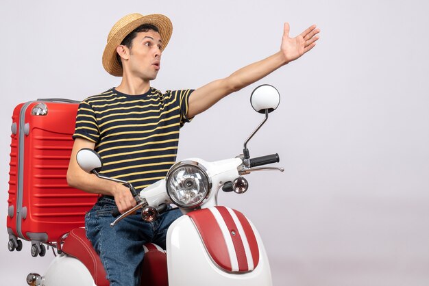 Vue de face du jeune homme avec chapeau de paille sur cyclomoteur atteignant la main