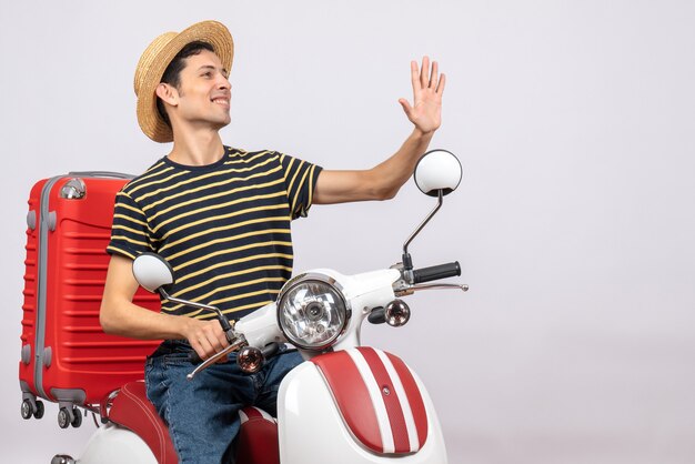 Vue de face du jeune homme avec un chapeau de paille sur un cyclomoteur hélant quelqu'un