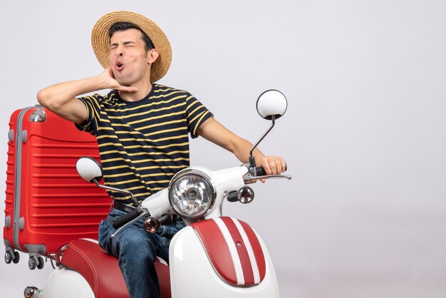 Vue de face du jeune homme avec un chapeau de paille sur un cyclomoteur tenant la gorge avec douleur