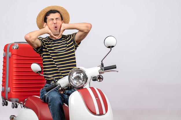 Vue de face du jeune homme avec un chapeau de paille sur un cyclomoteur tenant sa gorge avec douleur