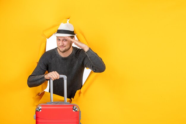 Vue de face du jeune homme avec un chapeau tenant un sac et disant bonjour dans un mur jaune déchiré