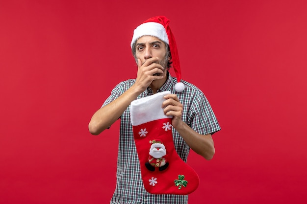 Vue De Face Du Jeune Homme Avec Chaussette De Noël Sur Un Mur Rouge Clair