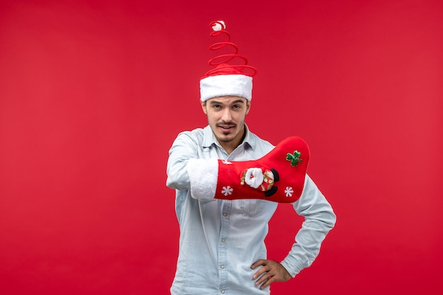 Vue de face du jeune homme avec chaussette de Noël sur mur rouge