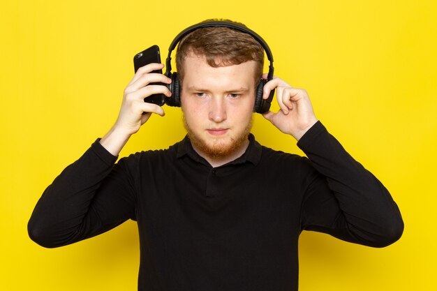 Vue de face du jeune homme en chemise noire, écouter de la musique via des écouteurs