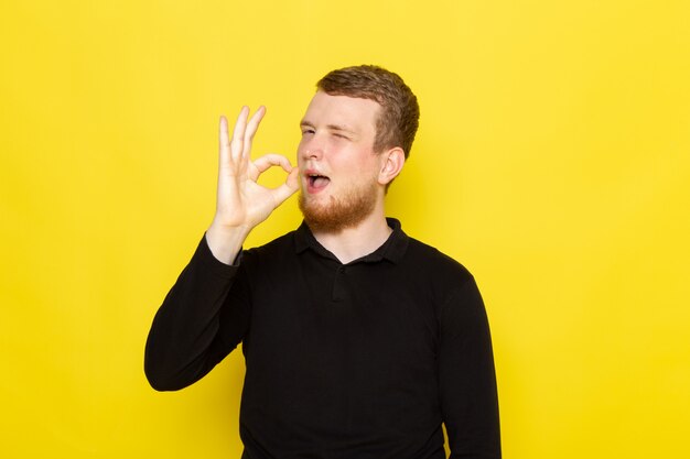 Vue de face du jeune homme en chemise noire posant avec une drôle d'expression