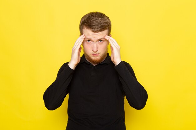 Vue de face du jeune homme en chemise noire posant avec une expression stressée