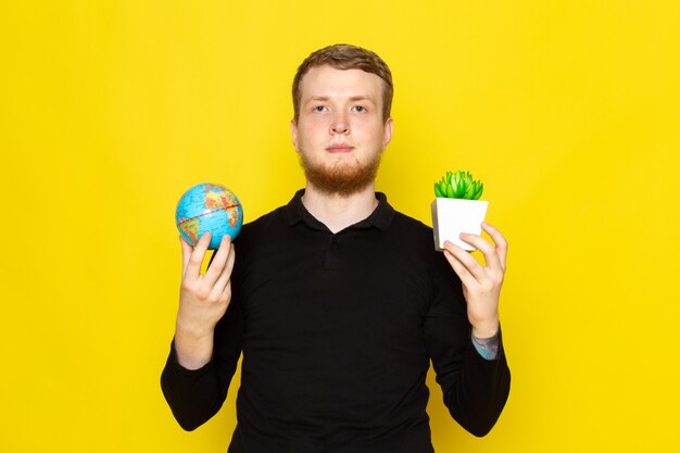 Vue de face du jeune homme en chemise noire tenant petit globe et plante