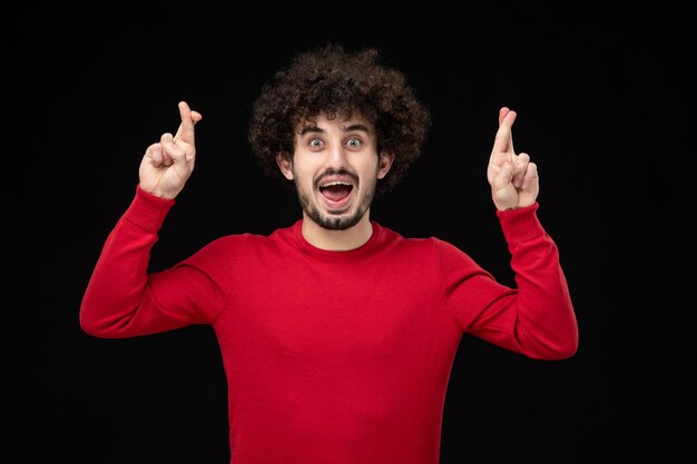 Vue de face du jeune homme en chemise rouge sur mur noir