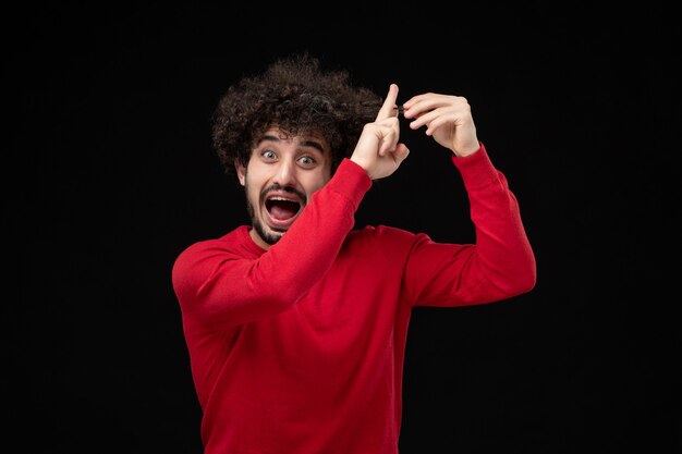 Vue de face du jeune homme en chemise rouge sur mur noir