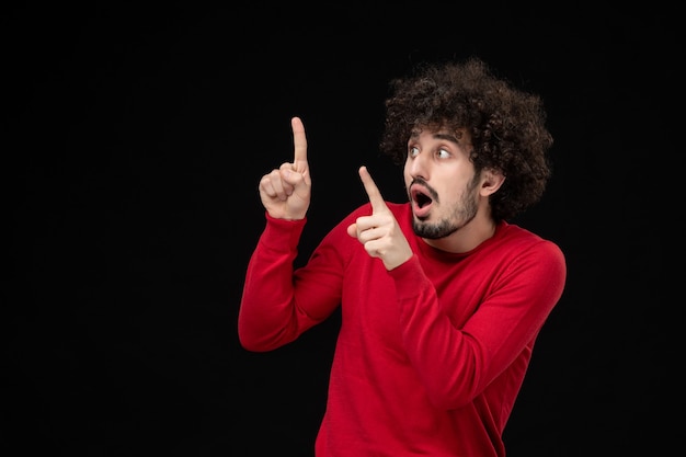 Vue de face du jeune homme en chemise rouge sur mur noir