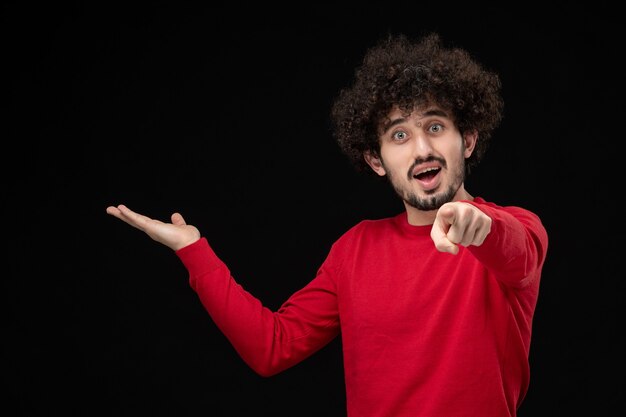 Vue de face du jeune homme en chemise rouge sur mur noir