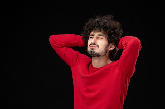 Vue de face du jeune homme en chemise rouge sur mur noir