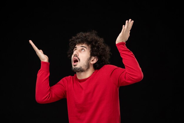 Vue de face du jeune homme en chemise rouge sur mur noir